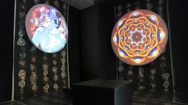 Two round video sculptures glow with kaleidoscopic imagery on a dark wall.
