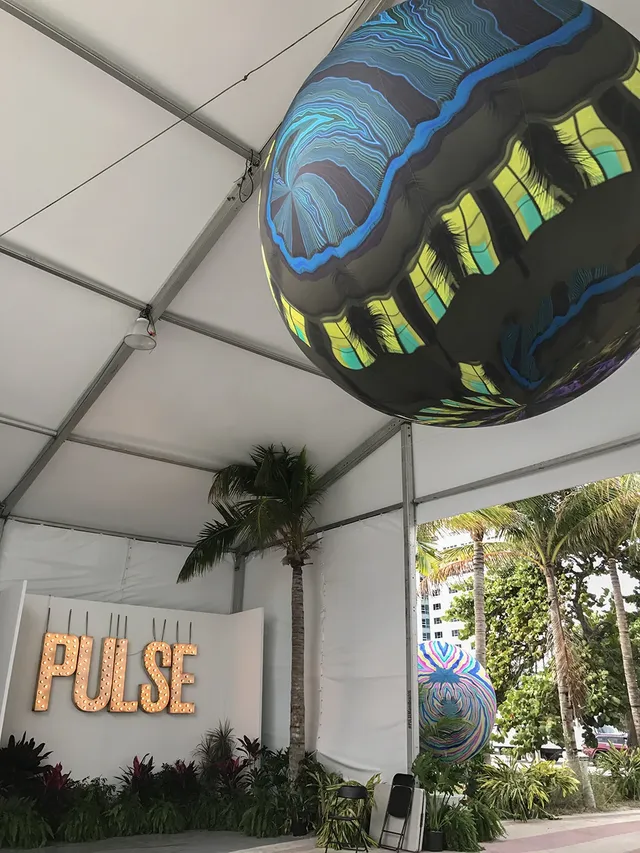 Large inflatable spheres printed with swirling blue and yellow imagery hang inside a white tent.