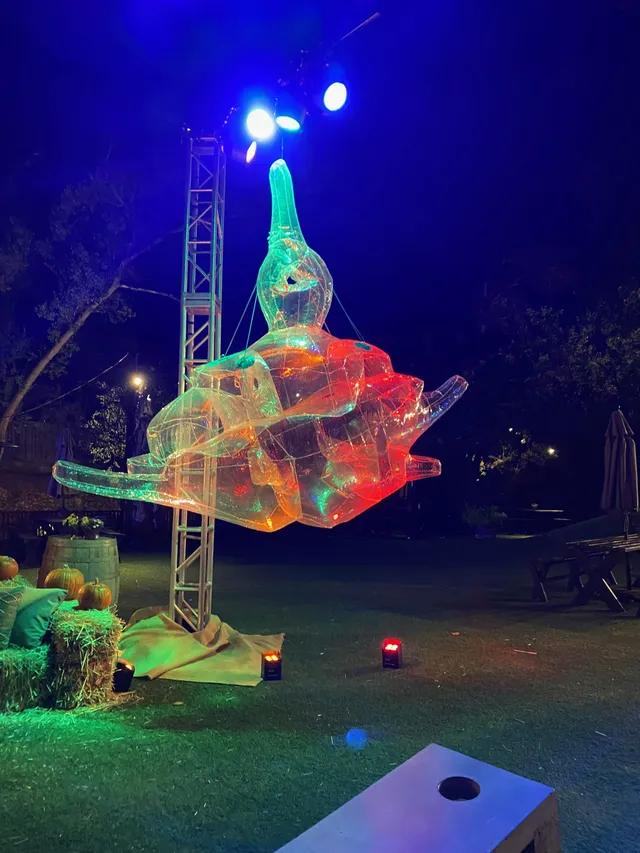 A tall translucent inflatable ship, lit green and orange, stands outdoors at night.